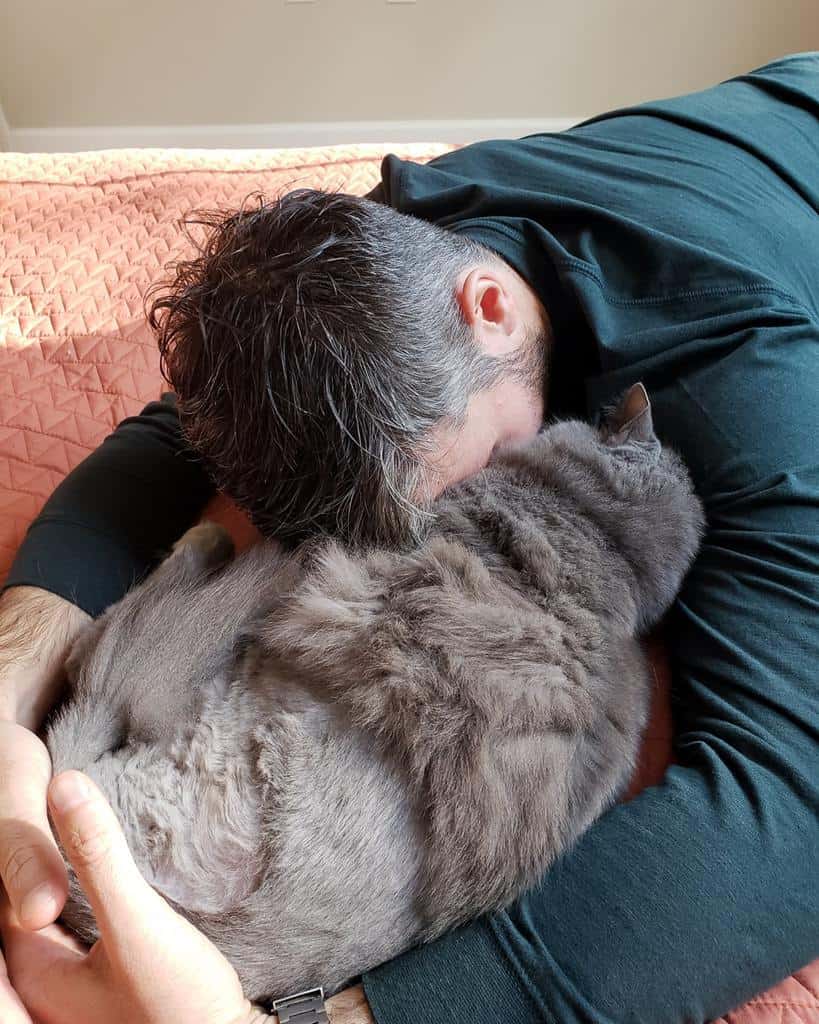 man cuddling grey cat who has only three legs from cancer