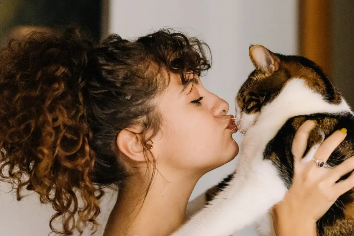 curly haired woman kisses cat on nose
