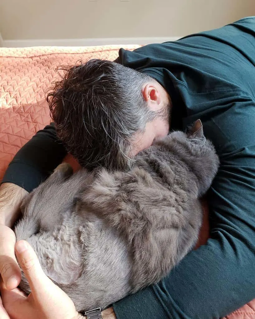 man cuddling grey cat who has only three legs from cancer